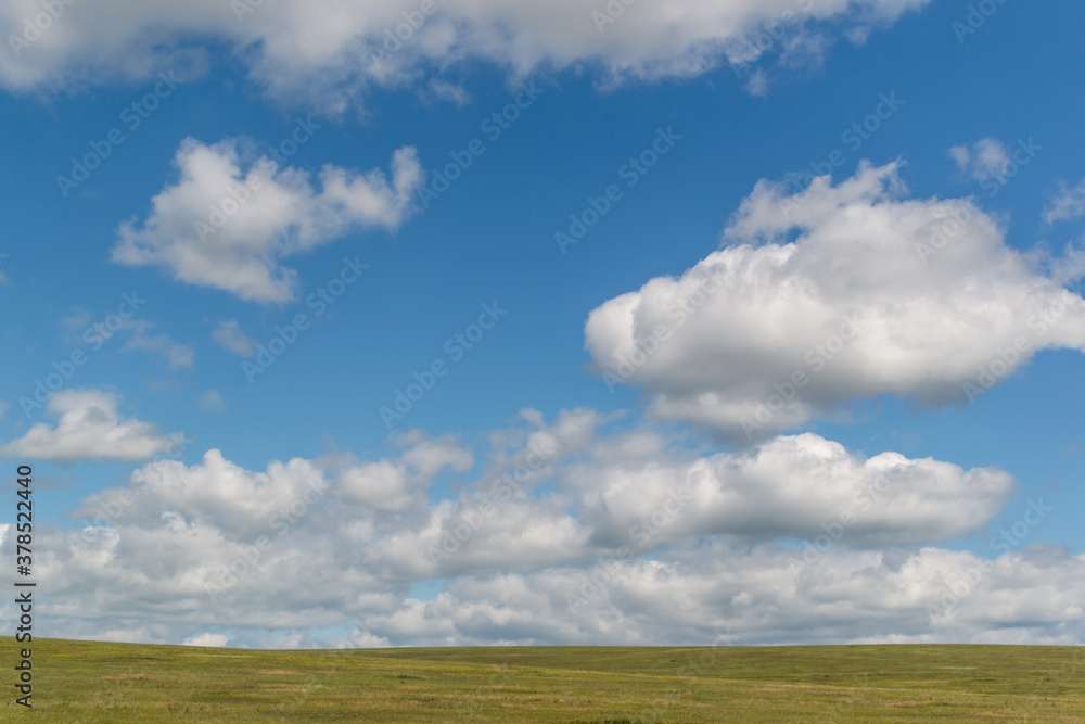 white fluffy clouds in bright blue sky with green field, open space
