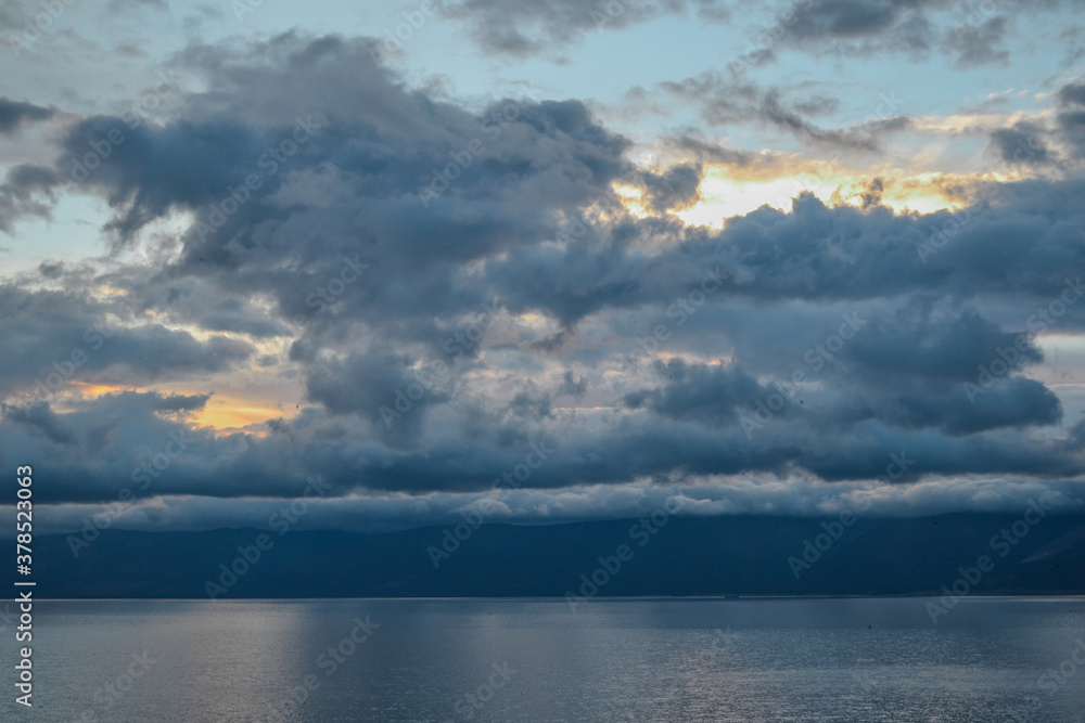 evening bright sunset with silvery gray blue clouds on lake baikal with a mountains ridge on the horizon