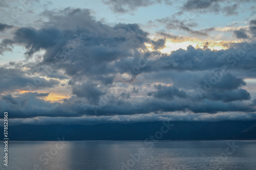 evening bright sunset with silvery gray blue clouds on lake baikal with a mountains ridge on the horizon © SymbiosisArtmedia