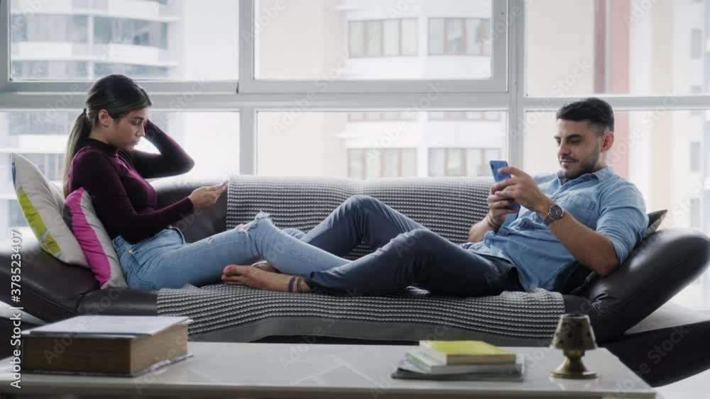 Young couple with smartphone at home. Man and woman ignoring each other, using cell phone. Husband and wife with mobile telephone on sofa. Bored partners and lifestyle Young couple with smartphone at home. Man and woman ignoring each other, using cell phone. Husband and wife with mobile telephone on sofa. Bored partners and lifestyle