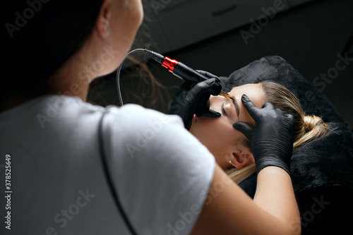 Beauty specialist in gloves applying brow tattoo