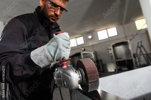 Industrial worker with angle grinder working and polishing stainless steel structure at workshop. photo