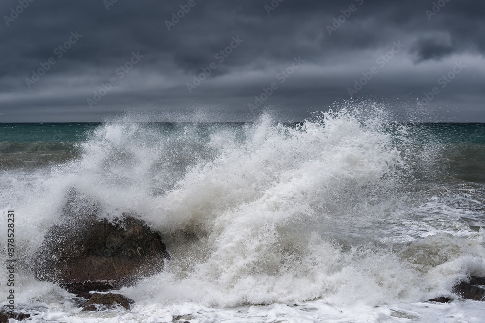 A large wave breaks on a rock during a storm on the Black sea in Crimea with a dark gloomy sky
