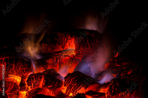 Red-hot coals in a fire with a blue flame on black