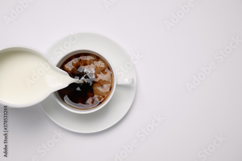 Canvastavla Pouring milk into cup of coffee on white background, top view