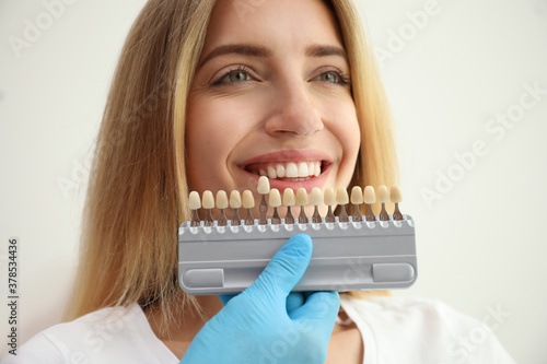 Doctor matching patient's teeth color with palette on white background, closeup. Cosmetic dentistry