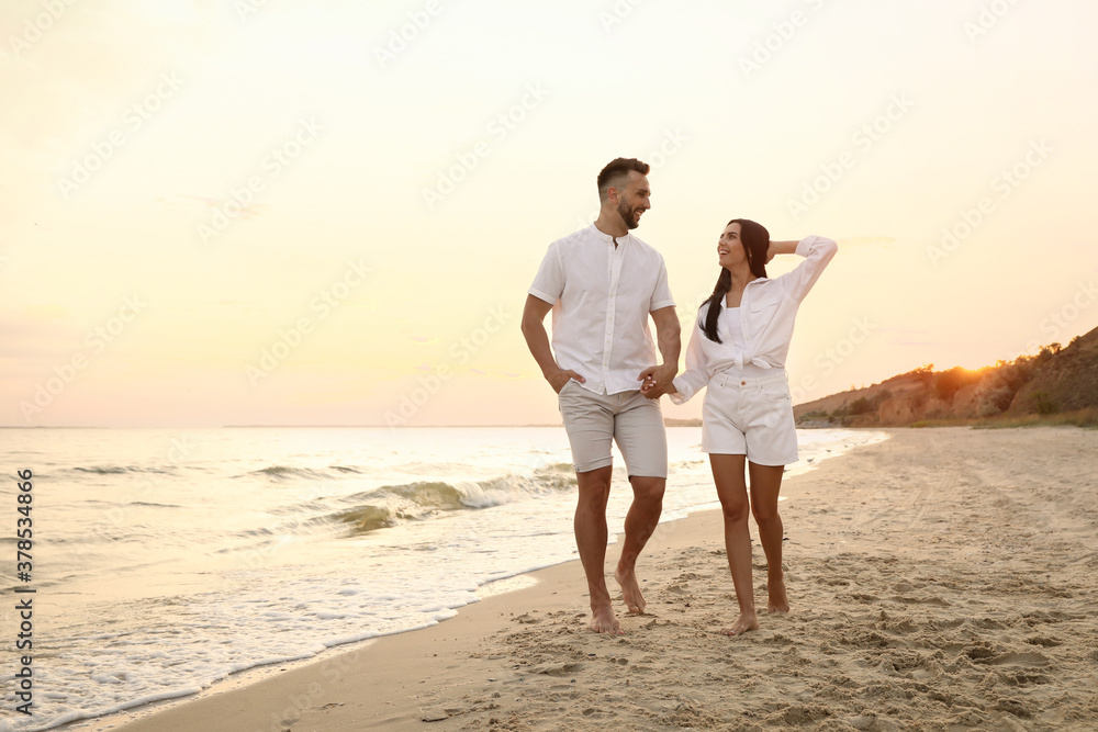 Happy young couple walking together on beach at sunset