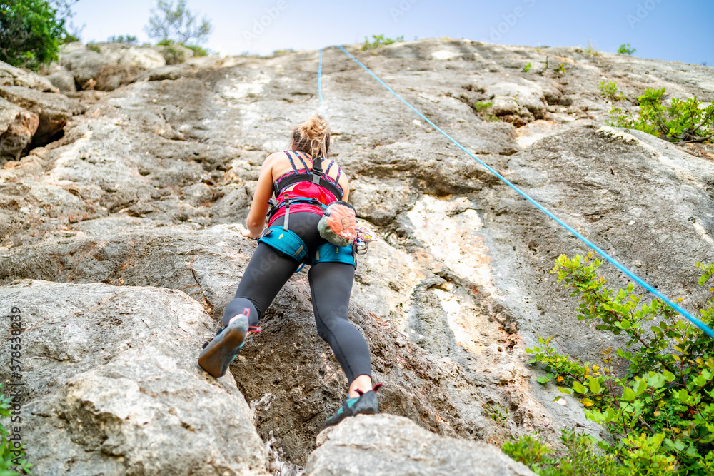 A woman climbing a steep rock in climbing harness