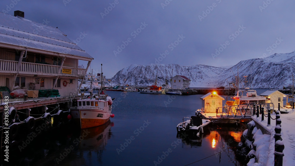 Blue hour photo before dark of illumineted harbor with fishing vessels in Honningsvag, Norway in winter time. Translation of signs: 
