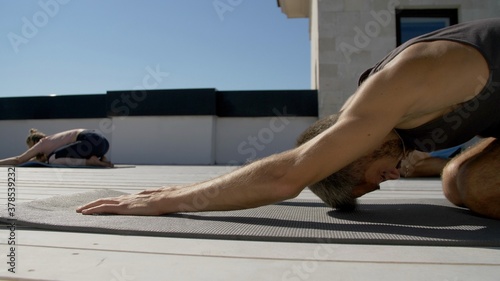 Portrait of Attractive caucasian man doing yoga exercises. Adult handsome bearded man doing fitness on rooftop. Outdoors meditation and wellness lifestyle concept on summer sunny day. © markwar