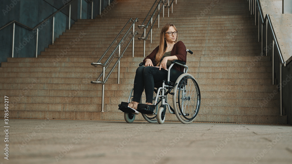 Obraz premium Hopeless young woman in the wheelchair in front of the inaccessible stairs. High quality photo