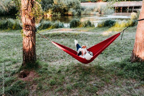back view of young woman relaxing with her dog in orange hammock. Camping outdoors. autumn season at sunset