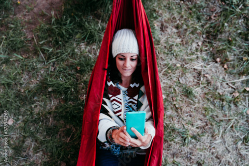 top view of young woman relaxing in hammock using mobile phone. autumn season. camping concept