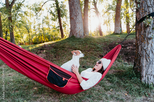 young woman relaxing with her dog in orange hammock. Camping outdoors. autumn season at sunset