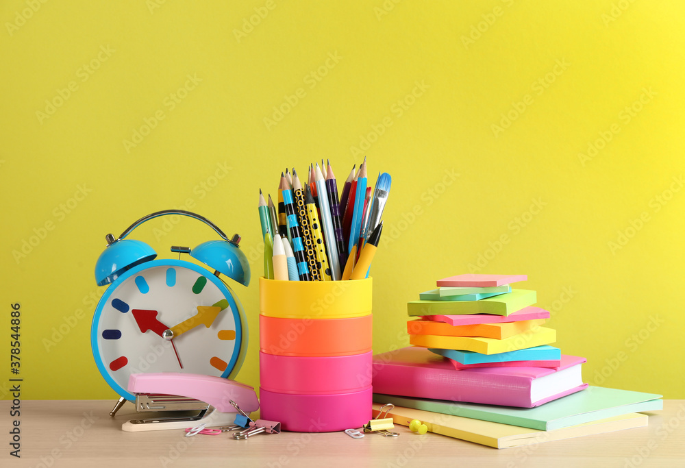 Set of school stationery and alarm clock on table against yellow background. Back to school
