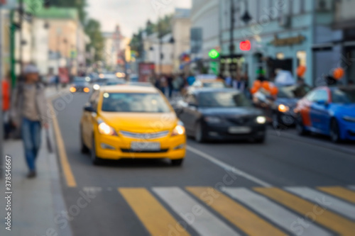 Defocused blured view of city street scene, urban traffic, yellow car before the pedestrian crossing next to the sidewalk Abstract urban background.