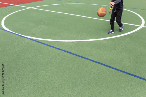 Artificial rubber-polymer coating of a modern multifunctional sports ground. A teenager plays a basketball.