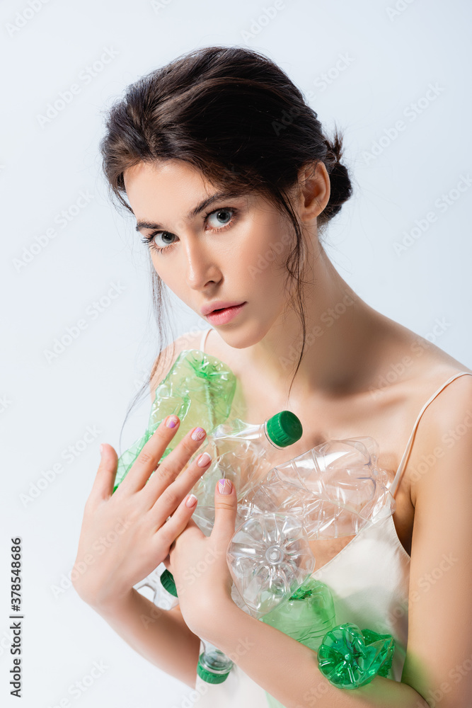 brunette woman holding plastic bottles and looking at camera isolated on white, ecology concept brunette woman holding plastic bottles and looking at camera isolated on white, ecology concept