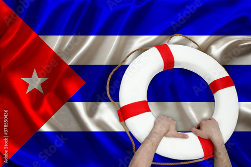 male hands hold on a white lifebuoy against the background of the silk national flag of Cuba, the concept of medical insurance, tourism, disaster, humanitarian assistance