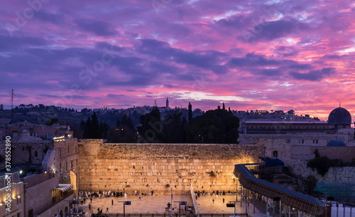 Jewish people praying Shacharit at the Western/Wailing Wall (Kotel) - holiest place in Judaism, and the Temple Mount with beautiful purple sunrise clouds; Jerusalem Israel photo