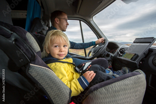 Cute toddler boy, kid sitting on the front seat in child seat on big camper van, smiling