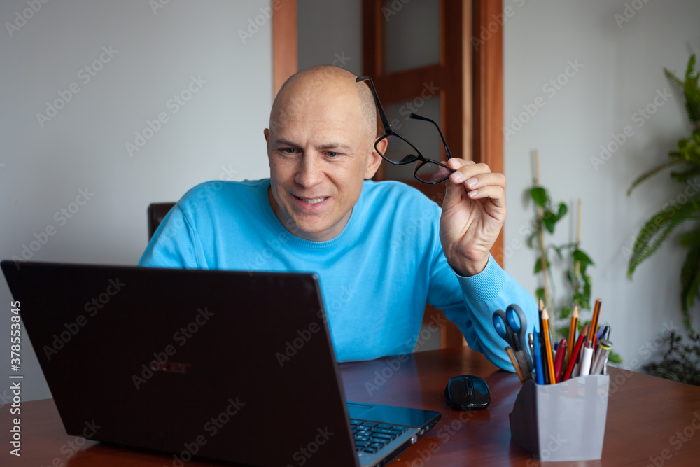 A cheerful man at home sits at a table with a laptop. A cheerful man at home sits at a table with a laptop.