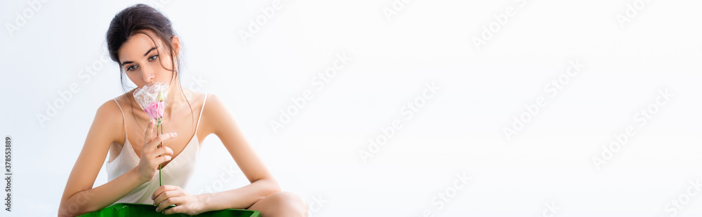 panoramic shot of brunette woman smelling pink flower in plastic wrap isolated on white, ecology concept panoramic shot of brunette woman smelling pink flower in plastic wrap isolated on white, ecology concept