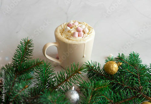 Celebrating Christmas. Hot Christmas drink. A cup of hot chocolate with marshmallows on a white marble background, branches of a Christmas tree, decorations and balls. View from above
