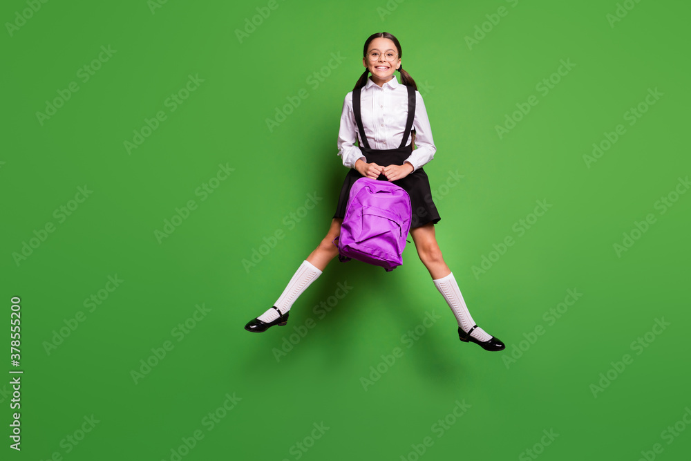 Photo portrait of happy schoolgirl jumping up with legs spread holding purple backpack isolated on vivid green colored background