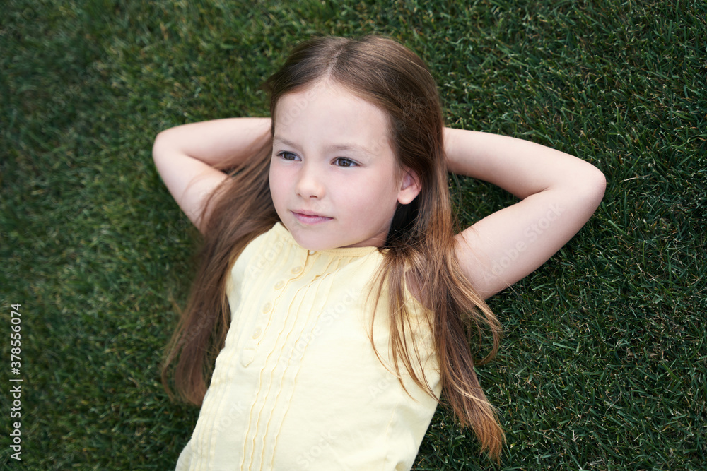Portrait of a cute little caucasian girl lying on a green grass, resting in park on a summer day Portrait of a cute little caucasian girl lying on a green grass, resting in park on a summer day