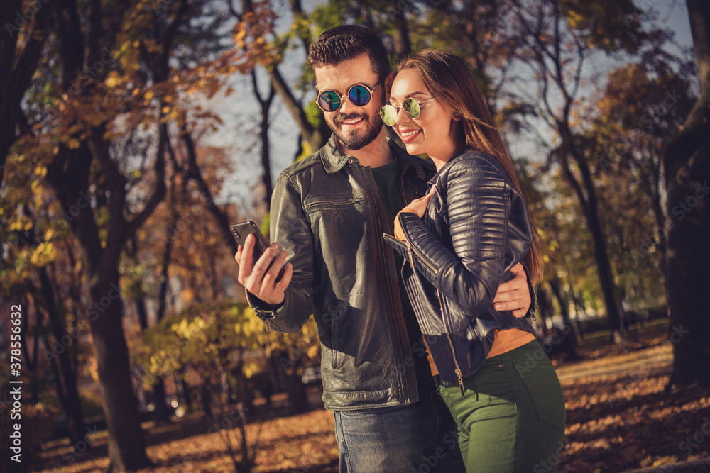 Photo of two people students guy girl read smartphone post in fall town october yellow forest park wear casual jacket