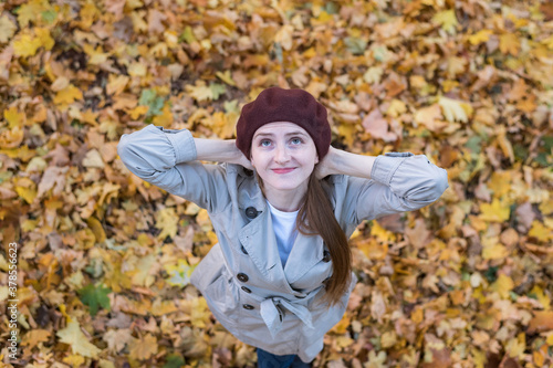 Cute young woman in beret on yellow autumn leaves background. Top view.