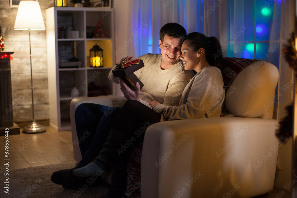 Obraz premium Couple in love on christmas day sitting on couch looking at magical present.