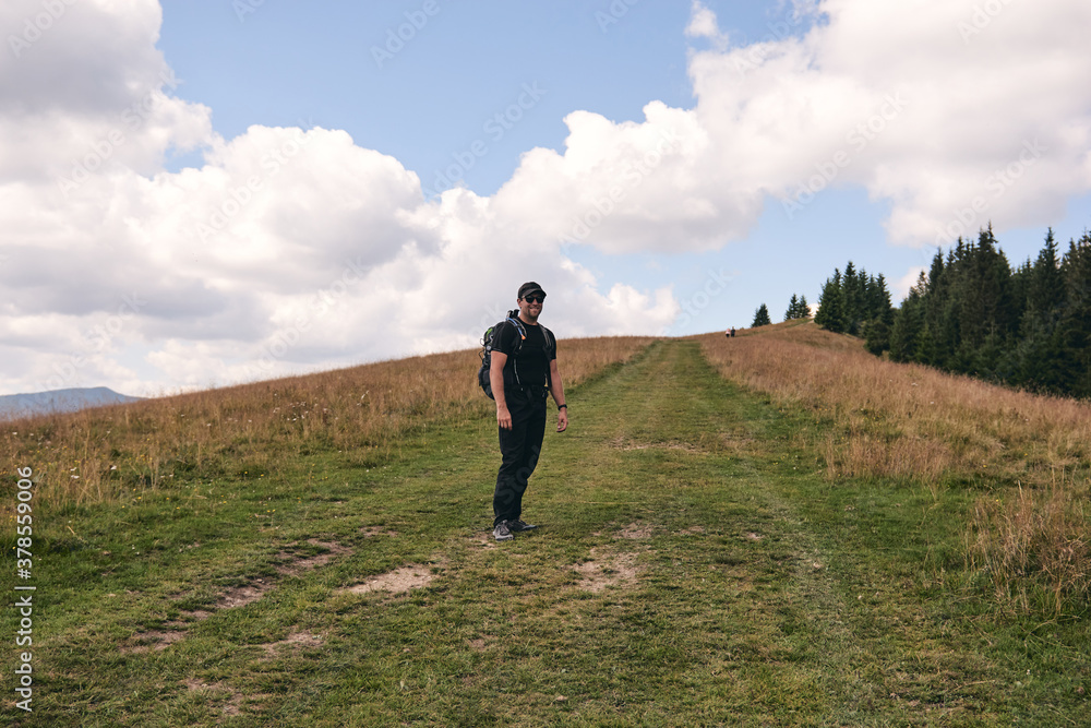 Man climbs uphill mountain. Sporty clothes and backpack. Hiking through forest in summer. A path between fir and pine-tree during a sunny day. Dark autumn forest. Hiking in wild mountain. Local Travel Man climbs uphill mountain. Sporty clothes and backpack. Hiking through forest in summer. A path between fir and pine-tree during a sunny day. Dark autumn forest. Hiking in wild mountain. Local Travel