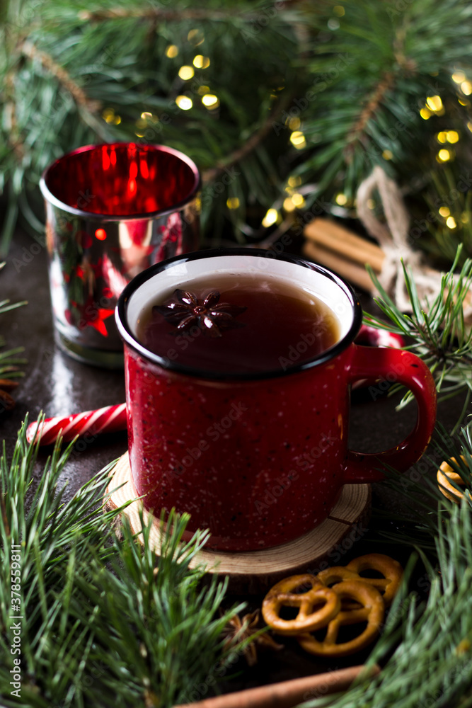 New year's tea party with spices. Red mug with tea surrounded by garlands, fir branches and spices New year's tea party with spices. Red mug with tea surrounded by garlands, fir branches and spices
