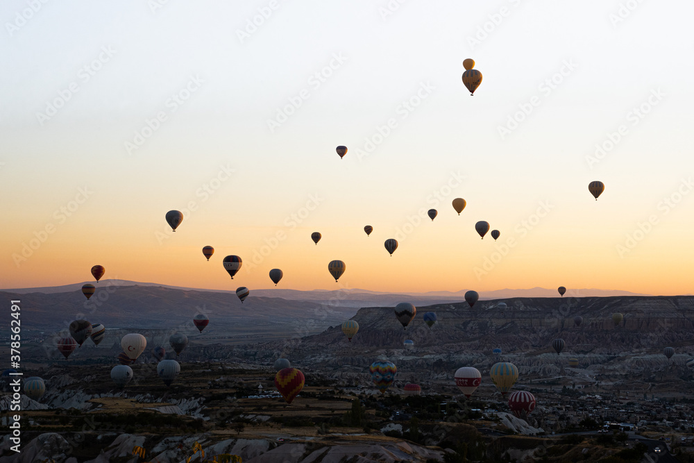 Colorful hot air balloons flying over Goreme National Park mountains at sunrise, Cappadocia, Turkey.