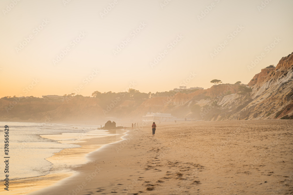 Falesia beach with golden sand and fog at sunset in the Atlantic Ocean. Olhos de Agua, Algarve, Portugal.