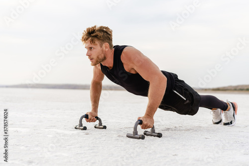 Photo of athletic young sportsman working out with push-up stops