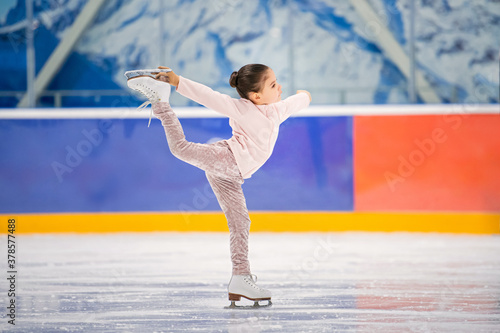 Canvas Print little girl figure skater in light pink tracksuit with smile skates on the ice on an indoor skating rink
