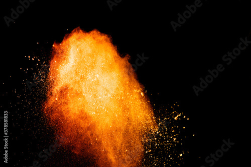 Abstract orange powder explosion. Closeup of orange dust particle splash isolated on black background.