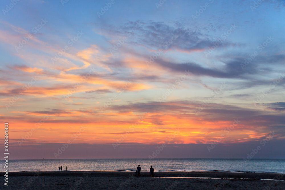 People at the beach looking at bizarre cloud formations creating an explosion of colours at sunset 