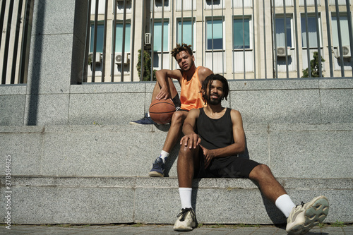 Image of african american guys resting with basketball after game