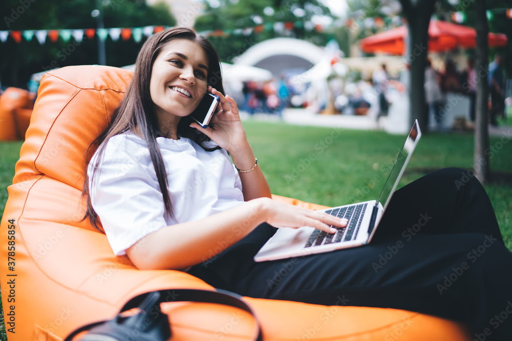 Smiling woman using laptop and talking on smartphone in park Smiling woman using laptop and talking on smartphone in park