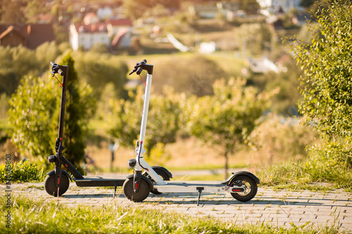 Two new black and white electric scooters stand in park and ready to go