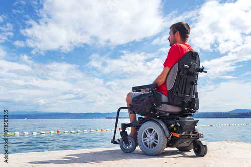 Фотография Man with muscular dystrophy on electric wheelchair outdoors looking at sea