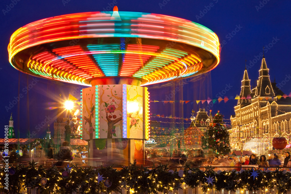 Fototapeta premium Luminous carousel at the New Year's fair in Moscow. The Red Square is decorated with Christmas trees, garlands and lights. On the right is the GUM shopping center, decorated with golden lights.