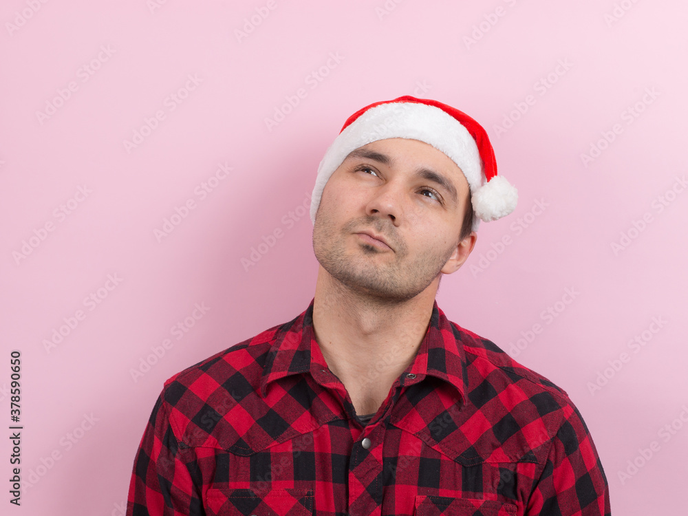 Emotions on the face, pensive, reflection, plan, idea. A man in a plaid rabbit and a Christmas red hat, on a pink background, copy space. Emotions on the face, pensive, reflection, plan, idea. A man in a plaid rabbit and a Christmas red hat, on a pink background, copy space.