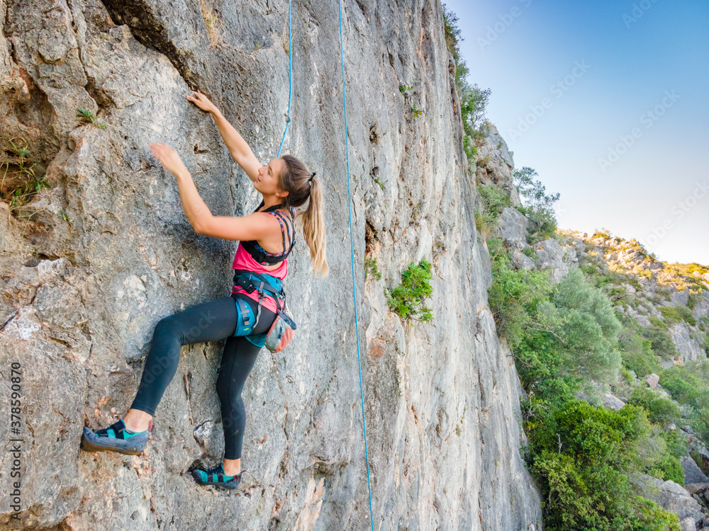 A woman in harness climbing a steep rock