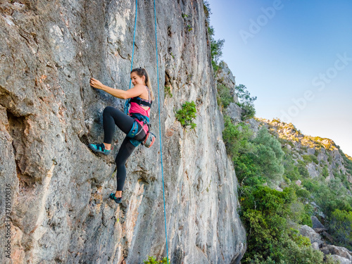 A woman in harness climbing a steep rock