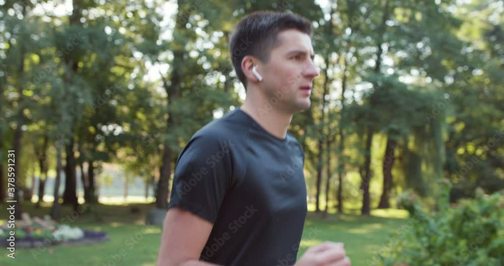 Handsome man using trendy earphones and smart watch. Sporty person training outside enjoying fresh nature. Healthy active lifestyle. Summer sunny day. Distance, heartbeat sport app Handsome man using trendy earphones and smart watch. Sporty person training outside enjoying fresh nature. Healthy active lifestyle. Summer sunny day. Distance, heartbeat sport app